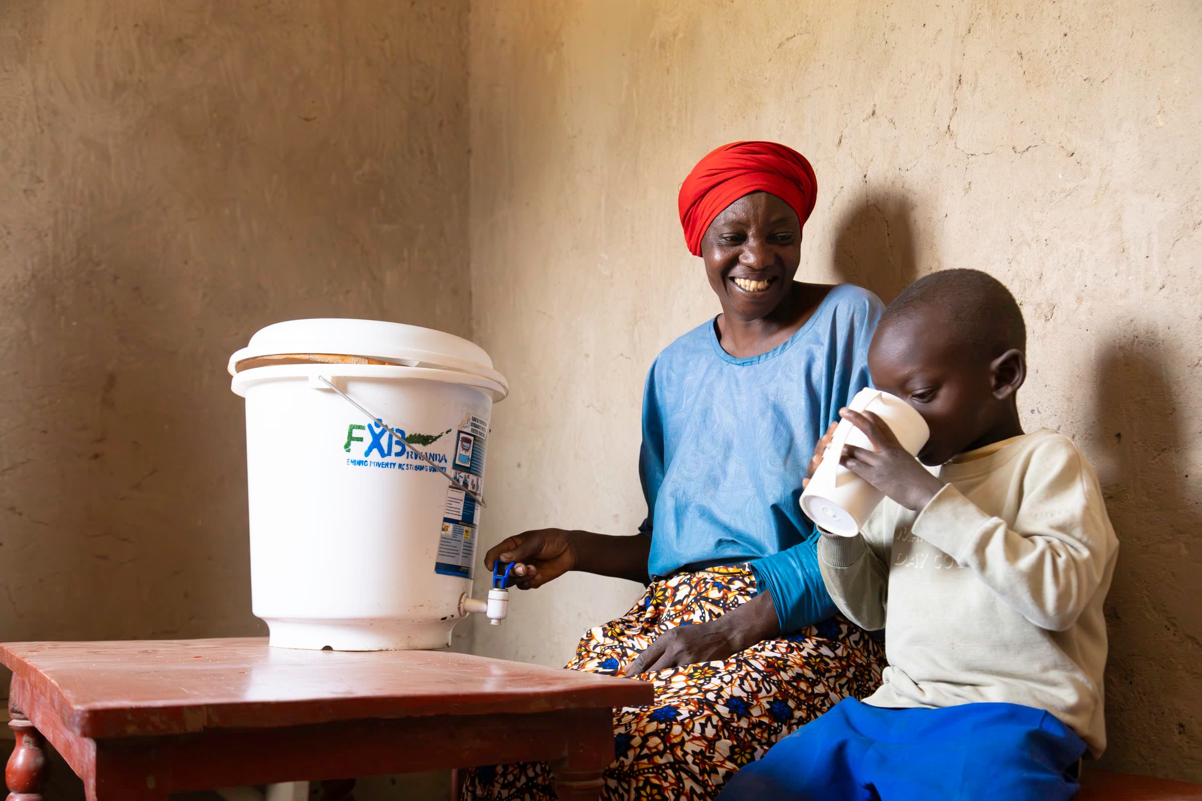 A child drinking clean water beside an FXB Rwanda household filter