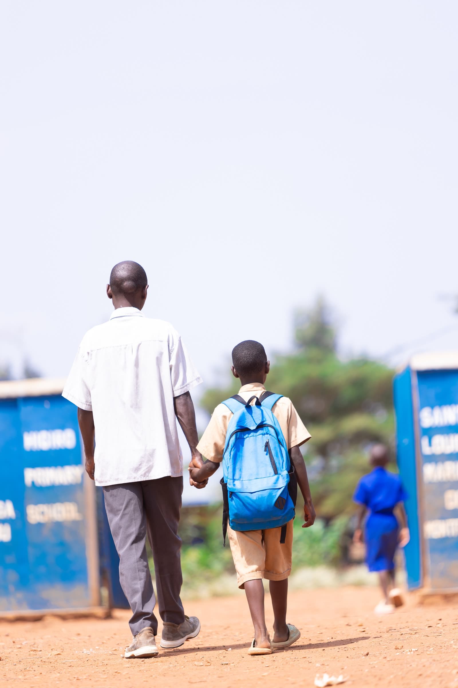 A man walking a boy in school uniform to the gates of his primary school